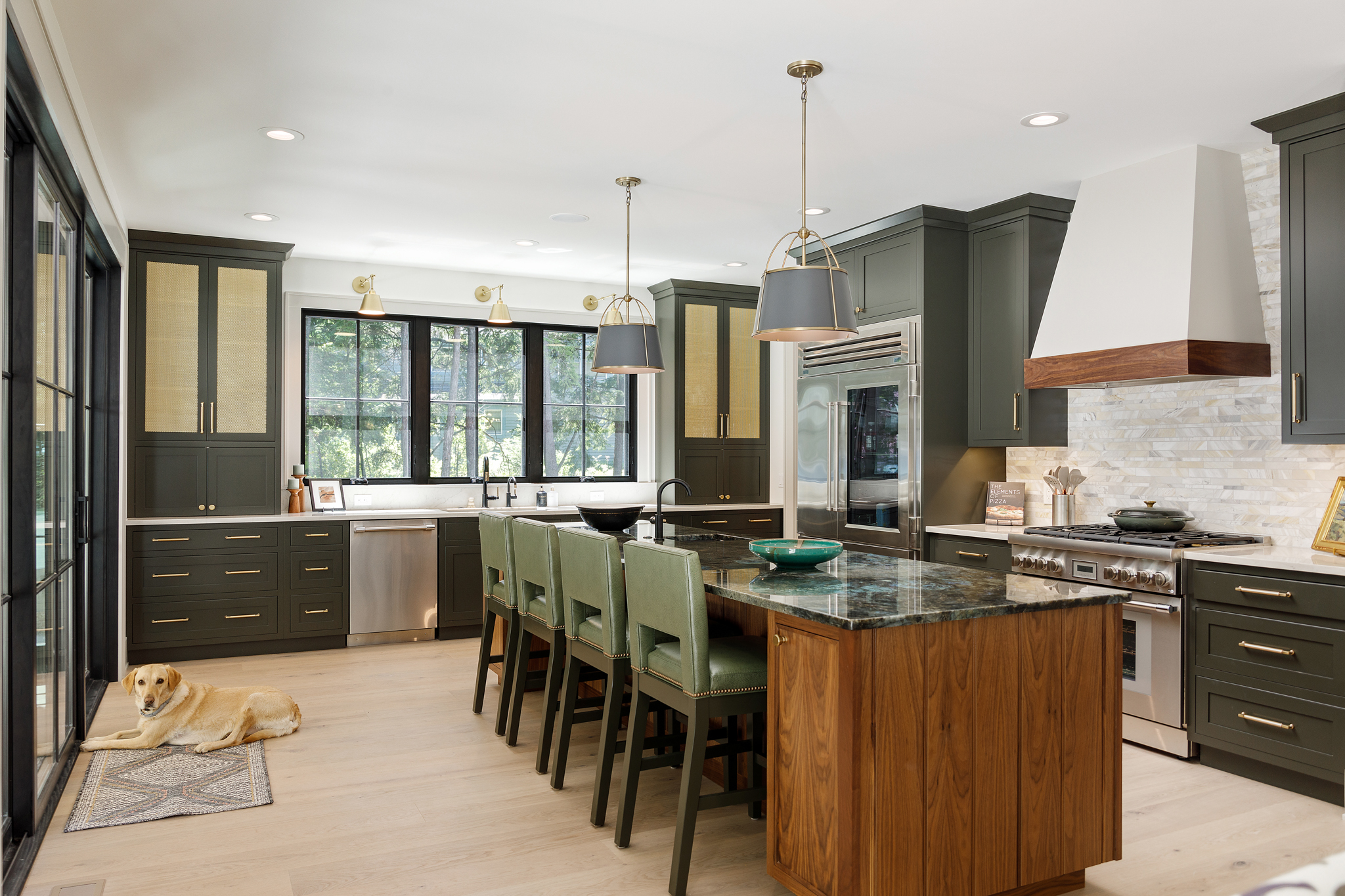 Open kitchen with dark green cabinetry, a walnut island with counter stools and a range hood with wood trim