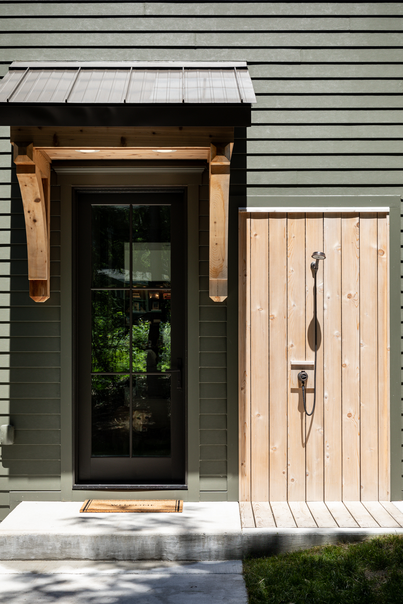 Glass entry door under a timber canopy, with dark green lap siding and a vertical wood board panel