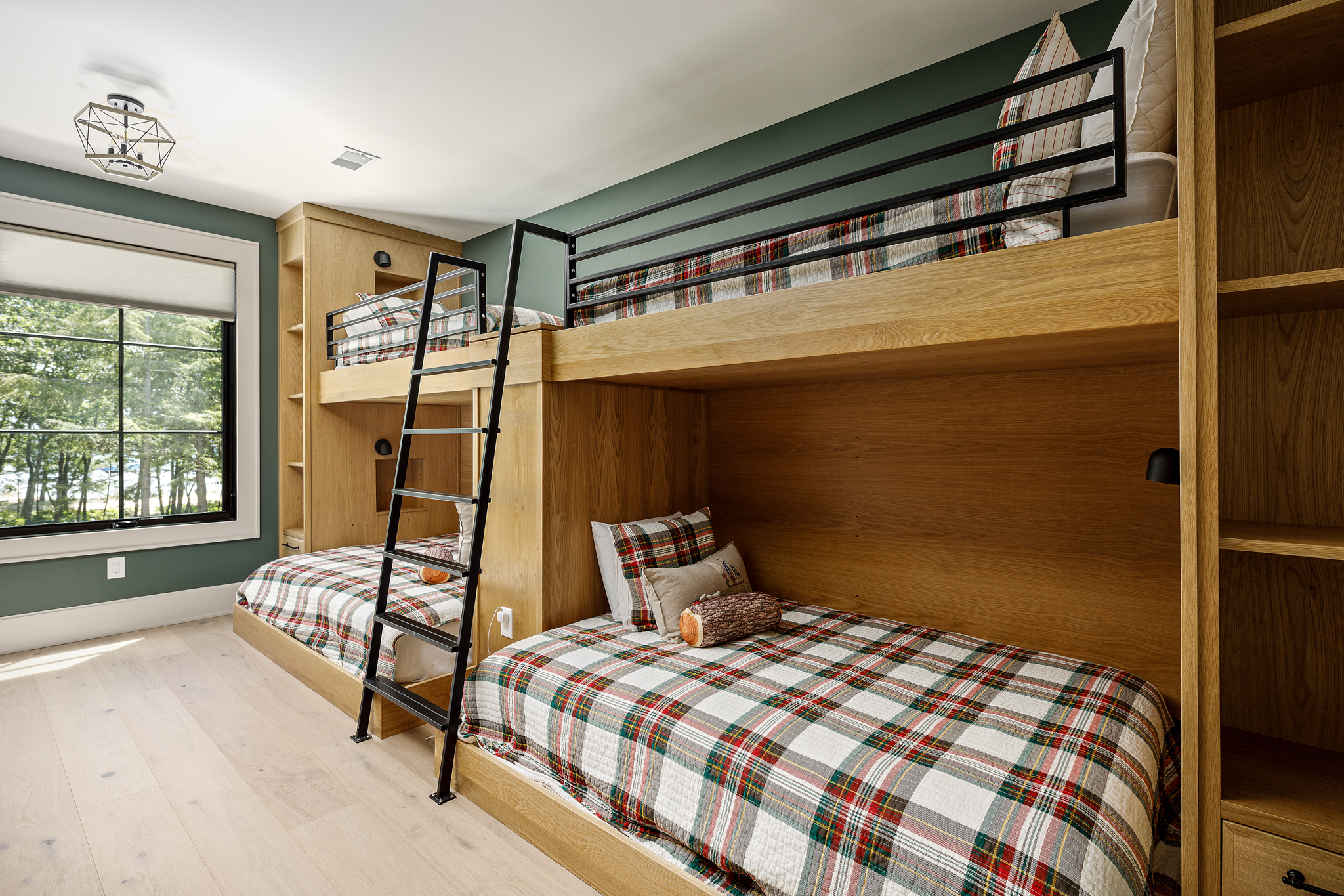 Built-in oak bunk beds with black ladders and plaid bedding in a green-walled bunk room
