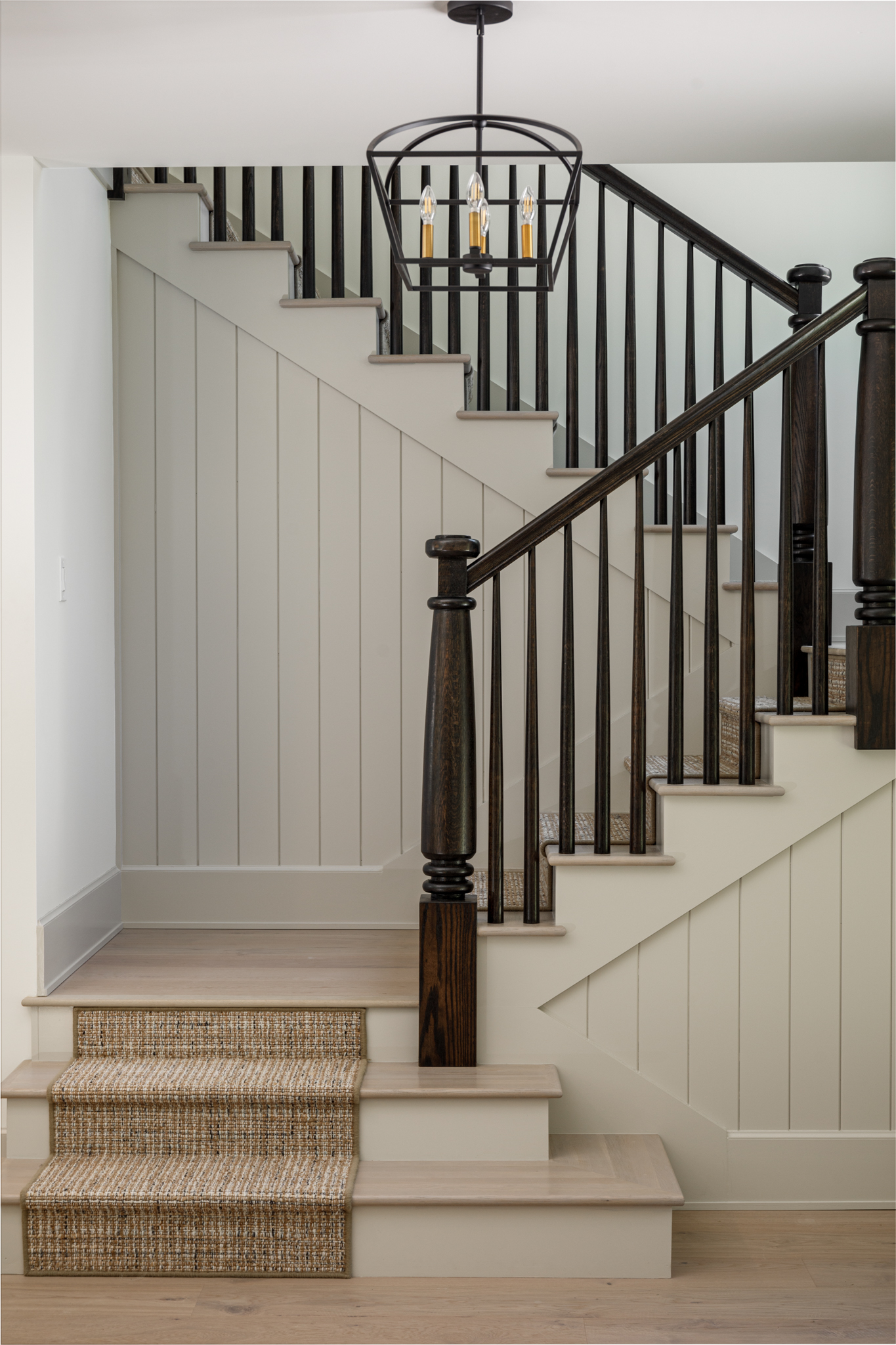Staircase with dark turned balusters and newel posts, a runner, and white board-and-batten walls
